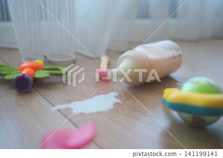 Baby toys and spilled milk on wooden floor in living room Baby toys and spilled milk on wooden floor in living room 141199141