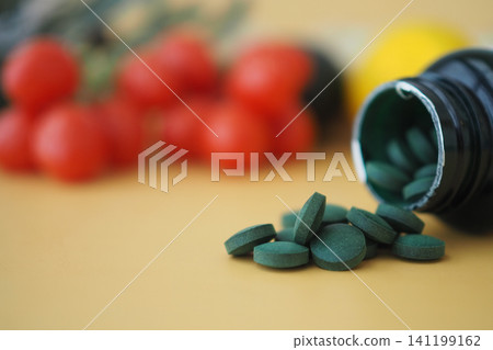 Green tablets spill from a bottle beside fresh vegetables Green tablets spill from a bottle beside fresh vegetables 141199162