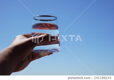 Holding a glass of water under a clear blue sky Holding a glass of water under a clear blue sky 141199233