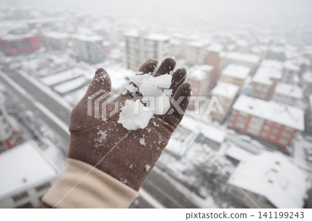 Hand holds snow overlooking city during winter season Hand holds snow overlooking city during winter season 141199243