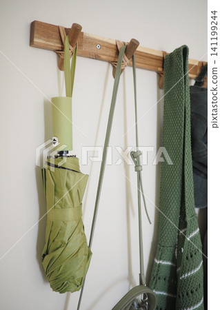Green umbrella hanging on a wall with other items nearby Green umbrella hanging on a wall with other items nearby 141199244