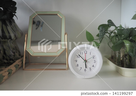 Clock and mirror on a shelf in a room Clock and mirror on a shelf in a room 141199297