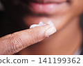 Applying skincare moisturizer on fingertip to treat skin 141199362