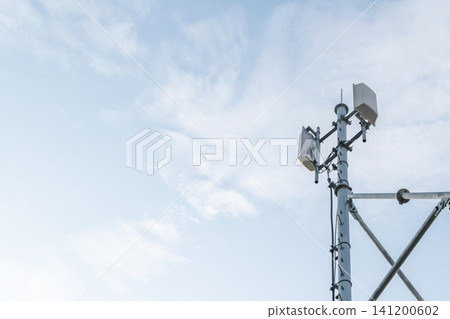 Cellular communication tower antenna panels standing against blue sky soft clouds representing wireless network infrastructure telecommunications signal transmission 141200602