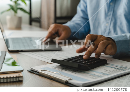 Close-up hands pressing a calculator over financial documents while reviewing figures beside a laptop, showing calculation workflow for accounting, budgeting, and report preparation. Close-up hands pressing a calculator over financial documents while reviewing figures beside a laptop, showing calculation workflow for accounting, budgeting, and report preparation. 141200778