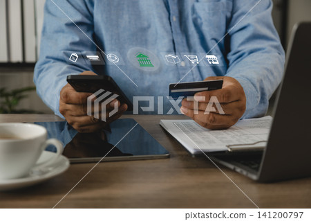 Man holds a smartphone and credit card at a desk, making an online shopping payment with digital banking icons, showing secure ecommerce transaction workflow for mobile finance and retail use. Man holds a smartphone and credit card at a desk, making an online shopping payment with digital banking icons, showing secure ecommerce transaction workflow for mobile finance and retail use. 141200797