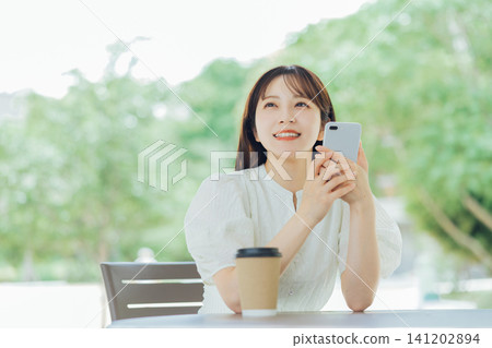 一位年輕女子在露臺上拿著智慧型手機。 141202894