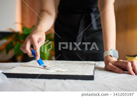 Woman making relief picture on canvas with plaster paste Woman making relief picture on canvas with plaster paste 141203197