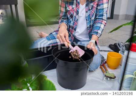 Woman adding clay pebbles to plant pot on patio Woman adding clay pebbles to plant pot on patio 141203198