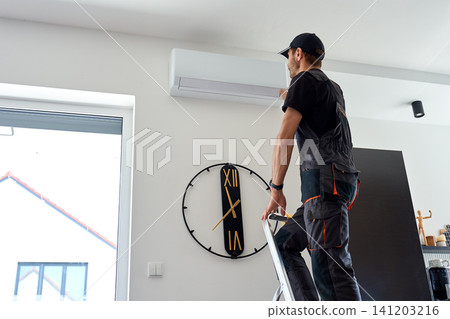 Air conditioner technician inspecting wall mounted AC unit in home Air conditioner technician inspecting wall mounted AC unit in home 141203216