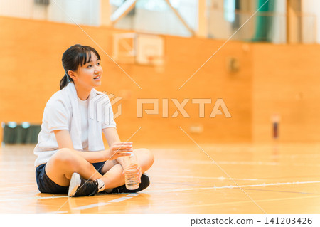 小學、國中和高中的女生穿著運動服在體育館喝瓶裝水補充水分 141203426