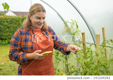 Young woman farmer working with smartphone in greenhouse garden Young woman farmer working with smartphone in greenhouse garden 141204262