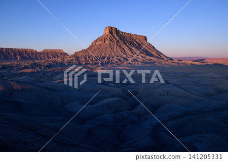 Majestic desert landscape featuring towering butte mountain in utah usa radiating peaceful emotional expression during sunrise over vast shadowed badland valleys Majestic desert landscape featuring towering butte mountain in utah usa radiating peaceful emotional expression during sunrise over vast shadowed badland valleys 141205331
