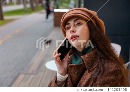 Portrait of young Caucasian lady enjoys a weekend stroll in the autumn city, holding her phone and checking messages while admiring the seasonal charm. Portrait of young Caucasian lady enjoys a weekend stroll in the autumn city, holding her phone and checking messages while admiring the seasonal charm. 141205408