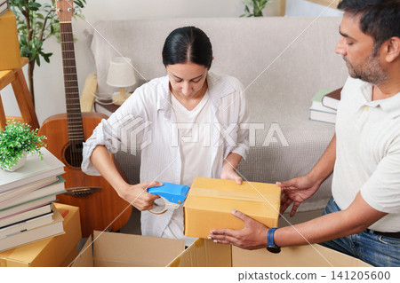 Indian couple sealing cardboard box with tape dispenser for relocation Indian couple sealing cardboard box with tape dispenser for relocation 141205600