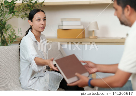 South Asian woman passing book to man while unpacking in new home South Asian woman passing book to man while unpacking in new home 141205617