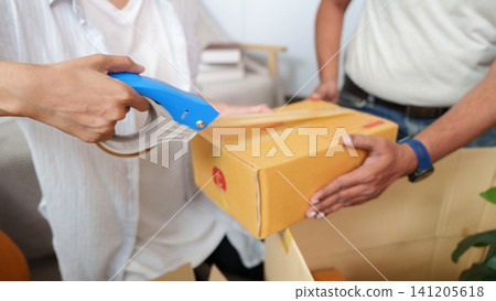 Close up of hands sealing cardboard box with tape dispenser for moving Close up of hands sealing cardboard box with tape dispenser for moving 141205618