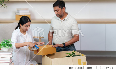 South Asian woman sealing cardboard box with tape dispenser for moving house South Asian woman sealing cardboard box with tape dispenser for moving house 141205644