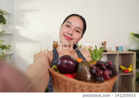 Smiling Asian woman holding basket of fresh fruits and vegetables for healthy lifestyle Smiling Asian woman holding basket of fresh fruits and vegetables for healthy lifestyle 141205653