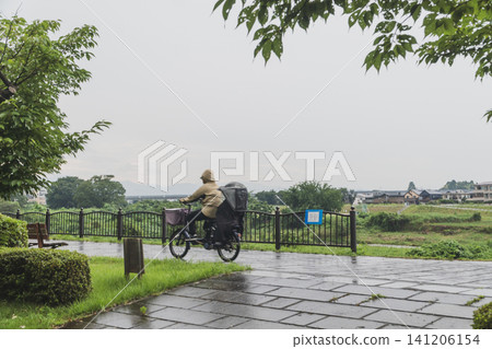 下雨天，一位女士穿著雨衣騎著腳踏車。 141206154