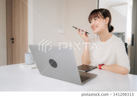Young happy asian woman enjoying modern lifestyle working from home office smiling while talking on mobile phone sitting at bright desk with laptop computer having cheerful conversation Young happy asian woman enjoying modern lifestyle working from home office smiling while talking on mobile phone sitting at bright desk with laptop computer having cheerful conversation 141206313