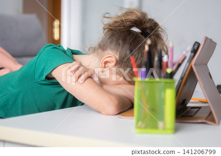 Tired schoolgirl resting her head on the desk during online learning at home Tired schoolgirl resting her head on the desk during online learning at home 141206799