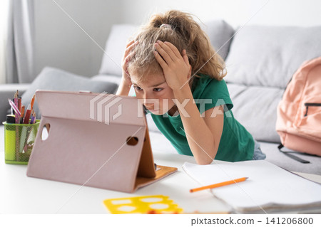 Stressed schoolgirl looking at a tablet while studying at home Stressed schoolgirl looking at a tablet while studying at home 141206800