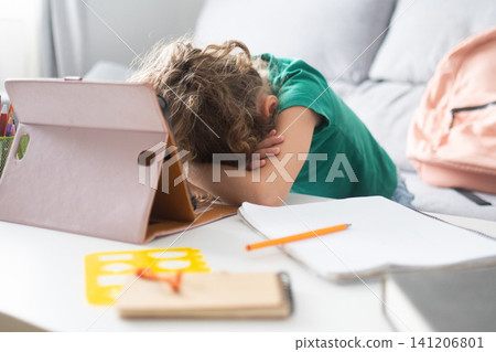 Tired schoolgirl resting her head on the desk during online learning at home Tired schoolgirl resting her head on the desk during online learning at home 141206801