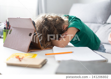 Tired schoolgirl resting her head on the desk during online learning at home 141206802