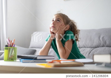 Thoughtful schoolgirl looking up while studying at home Thoughtful schoolgirl looking up while studying at home 141206804