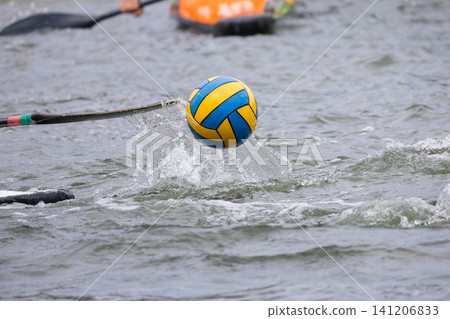 Canoe polo ball splashes above water surface as paddle strikes, with blurred kayakers in the background during an outdoor water sports competition Canoe polo ball splashes above water surface as paddle strikes, with blurred kayakers in the background during an outdoor water sports competition 141206833