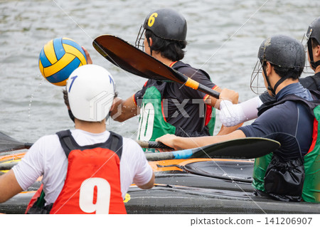 Canoe polo players in action, wearing helmets and paddling, as a water polo ball is thrown during a competitive match on a river or lake Canoe polo players in action, wearing helmets and paddling, as a water polo ball is thrown during a competitive match on a river or lake 141206907