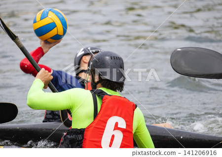 Two athletes engaged in canoe polo, one preparing to throw a ball while the other paddles, with water and kayaks visible in the background Two athletes engaged in canoe polo, one preparing to throw a ball while the other paddles, with water and kayaks visible in the background 141206916
