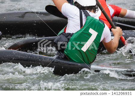 Canoe polo players in colorful jerseys paddle vigorously in a dynamic water setting, showcasing teamwork and skill during an intense match on a river Canoe polo players in colorful jerseys paddle vigorously in a dynamic water setting, showcasing teamwork and skill during an intense match on a river 141206931
