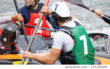 Canoe polo players in action, wearing helmets and paddling in a competitive match on a river, with splashes of water and colorful kayaks visible in the scene Canoe polo players in action, wearing helmets and paddling in a competitive match on a river, with splashes of water and colorful kayaks visible in the scene 141206940
