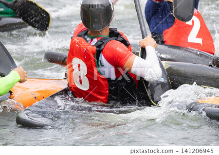 Canoe polo players in colorful jerseys maneuvering their kayaks on a river, with splashes of water and dynamic movement captured in the scene Canoe polo players in colorful jerseys maneuvering their kayaks on a river, with splashes of water and dynamic movement captured in the scene 141206945