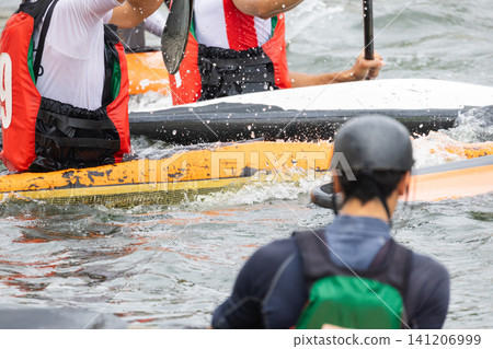 Canoe polo players in colorful life jackets engage in competitive action on a river, with splashes of water and kayaks visible in the dynamic scene Canoe polo players in colorful life jackets engage in competitive action on a river, with splashes of water and kayaks visible in the dynamic scene 141206999