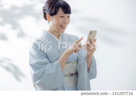 A woman in a kimono using a smartphone A woman in a kimono using a smartphone 141207718