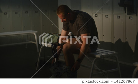 Adaptive Athlete Undressing in Locker Room Showing Modern Leg Prosthesis Adaptive Athlete Undressing in Locker Room Showing Modern Leg Prosthesis 141207967
