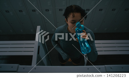 Female Athlete Dressing and Staying Hydrated in Dark Dressing Room Female Athlete Dressing and Staying Hydrated in Dark Dressing Room 141208223
