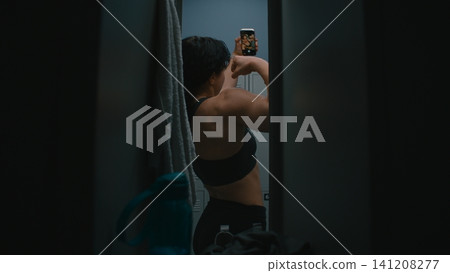 Confident Young Female Athlete Opening Door, Taking Smartphone, Posing For Selfie by Flexing Biceps Confident Young Female Athlete Opening Door, Taking Smartphone, Posing For Selfie by Flexing Biceps 141208277