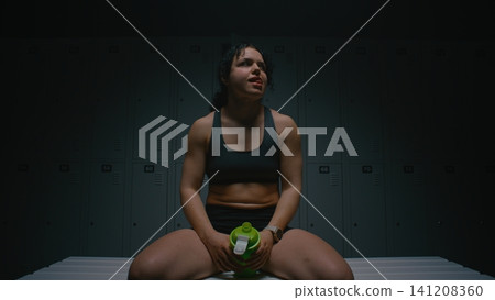 Exhausted Yet Satisfied Athlete Drinking Protein Shake in Moody Locker Room Exhausted Yet Satisfied Athlete Drinking Protein Shake in Moody Locker Room 141208360
