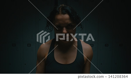 Determined Sportswoman with Intense Glare in Dark Dressing Room Determined Sportswoman with Intense Glare in Dark Dressing Room 141208364