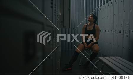 Sporty Female Athlete Focusing and Using on Earbuds in Dressing Room Sporty Female Athlete Focusing and Using on Earbuds in Dressing Room 141208386