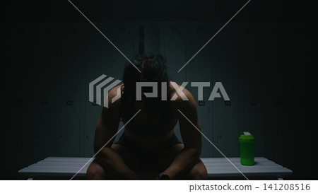 Pensive Sportswoman Relaxing and Stretching Shoulders in Moody Dressing Room Pensive Sportswoman Relaxing and Stretching Shoulders in Moody Dressing Room 141208516