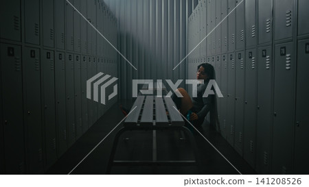 Exhausted Woman Athlete Sitting on Floor in Empty Gym Locker Room Exhausted Woman Athlete Sitting on Floor in Empty Gym Locker Room 141208526