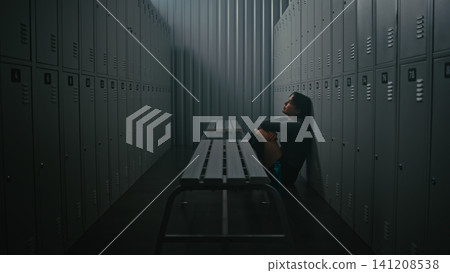 Exhausted Woman Athlete Sitting on Floor in Empty Gym Locker Room Exhausted Woman Athlete Sitting on Floor in Empty Gym Locker Room 141208538