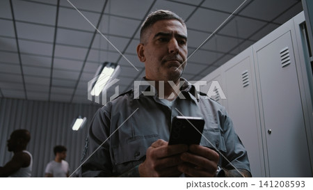 Focused Tattooed Airport Security Officer Concentrates on Typing Message at Locker Room After Work Focused Tattooed Airport Security Officer Concentrates on Typing Message at Locker Room After Work 141208593