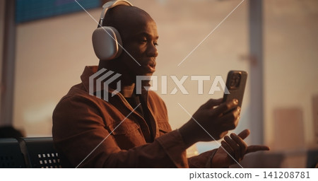 Male Professional Using Smartphone and Headphones for Video Meeting at Airport Male Professional Using Smartphone and Headphones for Video Meeting at Airport 141208781