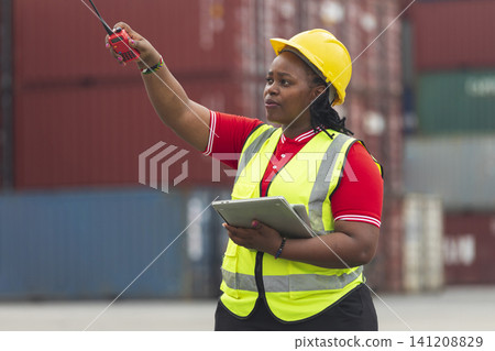Black foreman woman worker checking stock at container yard, holding laptop computer operate loading containers. Logistics import export shipping concept. 141208829